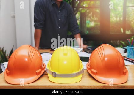 Close up of a helmets on the desk with architect working with blueprint construction project in home office. Stock Photo