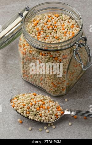Glass jar and a spoon with raw uncooked pearl couscous tricolore close up Stock Photo
