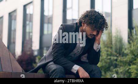 Suffering anxious worried irritated Indian business man feeling bad headache frustrated problem businessman employer manager entrepreneur in city Stock Photo