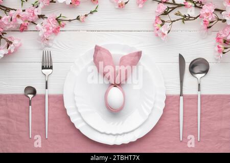 Easter lunch or brunch invitation. Festive table setting with pink spring flowers, cutlery. Bunny made of linen napkin and egg. Happy Easter holiday c Stock Photo