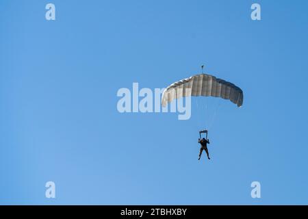 Silhouette of a parachutist descending with a white parachute Stock Photo