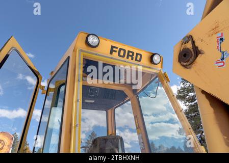 Looking up at the cab of a yellow Ford backhoe, blue sky with clouds in the background. Stock Photo