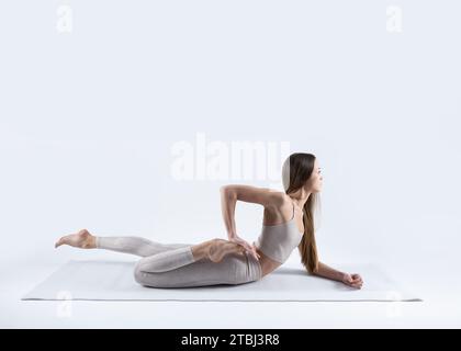 beautiful young athletic woman doing arda bhekasana half frog pose on a white mat with a white background 2tbj3r8