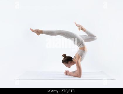 beautiful young athletic woman doing pincha mayurasana (forearm stand) on a white mat with a white background Stock Photo