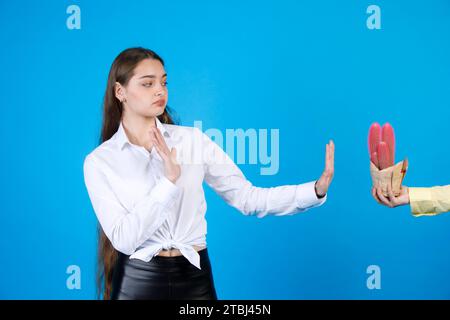 Vexed, scared girl making stop gesture for anonymous hand presenting colored cacti in studio. Stock Photo