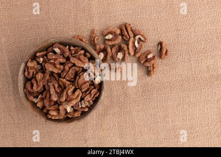walnuts in wooden bowl close-up on burlap fabric, roasted nuts on sacking with copy space, snack food concept, vegan meal Stock Photo