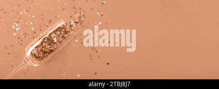 Champagne glass with star shaped sequins on a Peach Fuzz background. Party, christmas, new year, celebration concept. banner. Top view. Color of the y Stock Photo
