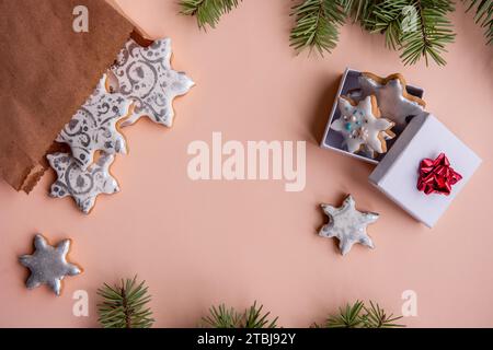 On peach fuzz isolated background lie craft bag with silver gingerbread cookies in shape of snowflake for Christmas. Top view of still life with green Stock Photo