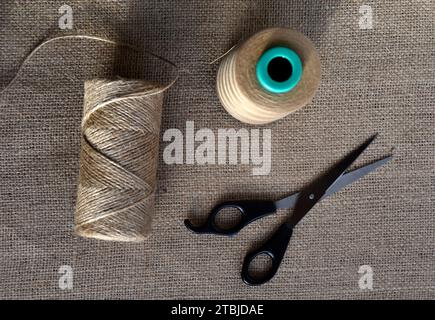 Yellow skeins of thread and scissors on a background of burlap. Yellow coarse cloth threads and scissors. Stock Photo