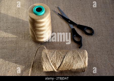 Yellow skeins of thread and scissors on a background of burlap. Yellow coarse cloth threads and scissors. Stock Photo