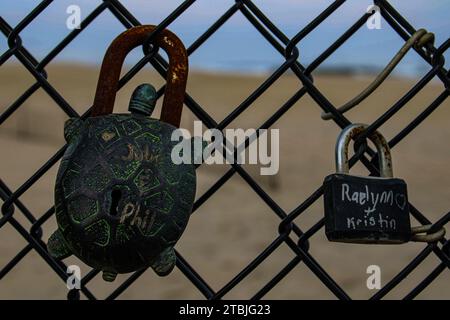 A close-up view of two metal locks securely attached to an iron fence on a beach shoreline Stock Photo