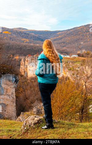 woman with long red hair on the top of a mountain admires the autumn landscape. Travel and tourism. Stock Photo