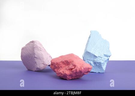 3 paint stones or pebbles in pink, salmon and blue pastel shades isolated on a white and violet background. Minimal still life and vibrant photography Stock Photo