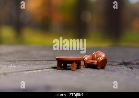 Miniature arm-chair and coffee table figurines arranged on a tree stump in the heart of the forest. Creative city break concept. Stock Photo