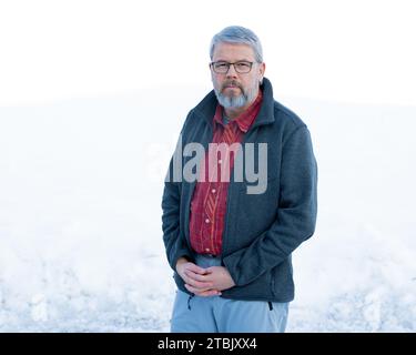 Man, 56 years, grey hair and beard, standing outside in winter with snow in background, Stock Photo