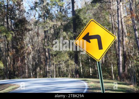 A yellow road sign of the left turn on a road Stock Photo