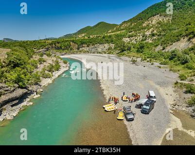 White water rafting.  Vertical drone view  of a group cars, yellow rafts and people ready to float on blue-green river Vjosa, Albania. Stock Photo
