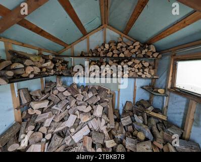 A stack of logs is neatly arranged against the side of a wooden shed, ready to be burned Stock Photo