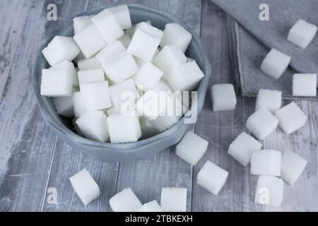 Sugar cubes in blue ceramic bowl on gray wooden background. Stock Photo