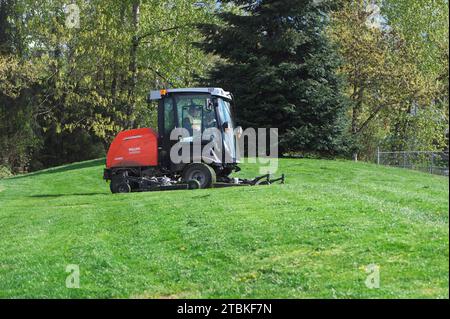 Male maintenance worker cutting the grass with a ride-on lawn mower at at a local park. Maple Ridge, B. C., Canada. Stock Photo