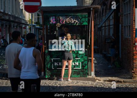 LX Factory, Lisbon, Portugal.  Young woman buying ice cream at a kiosk at the north entrance to the Factory.  The LX Factory is a refurbished 23,000 square-meter industrial park that has become a hub of art, multimedia, music shops, food and entertainment 3k (1.8 miles) west of the Lisbon city center. Stock Photo