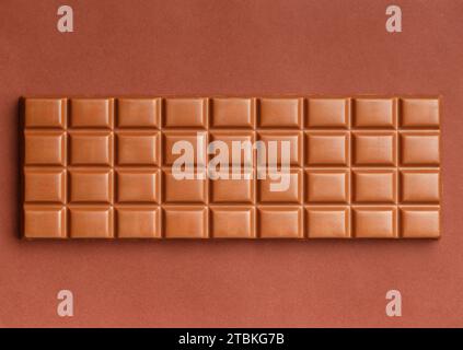 Large whole chocolate bar on brown background, top view. Milk chocolate isolated. Stock Photo