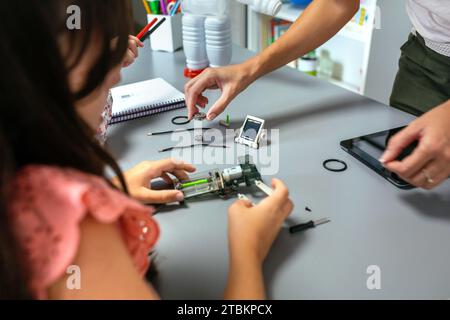 Female teacher helping girl students to assemble pieces of machine in a robotics class Stock Photo