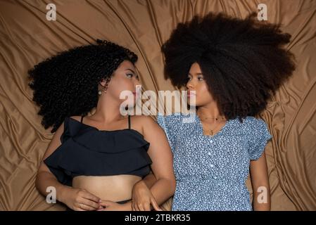 Half-closed portrait of two women lying down looking at each other. Solid friendship concept. Stock Photo