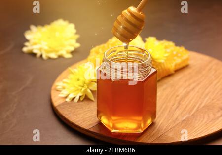 Natural honey dripping from dipper into glass jar on table under sunlight Stock Photo