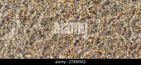 A background of sand, small pebbles and flowing waves on the sea beach. Summer vacation and coastal nature concept Stock Photo