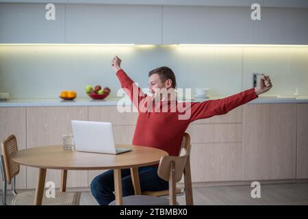 Smiling pleased happy man freelancer stretching arms in satisfaction, accomplishment of work ending Stock Photo