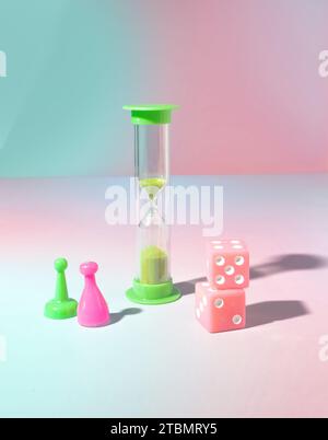 Green Sand Timer, Board Games Pawns, and Pink Dice on a Pastel Blue and Pink Background, Game Night Stock Photo