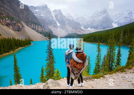 Lake Moraine during a cold snowy day in Canada, turquoise waters of Moraine Lake with snow at Banff National Park Canadian Rockies. Young couple men and women standing by a lake in Canada Stock Photo