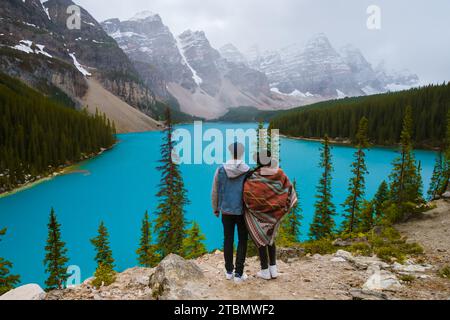 Lake Moraine during a cold snowy day in Canada, turquoise waters of Moraine Lake with snow at Banff National Park Canadian Rockies. Young couple men and women standing by a lake in Canada at sunrise Stock Photo