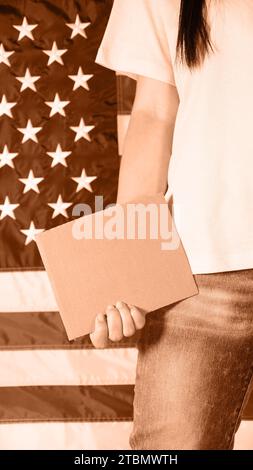 Young woman holding blank sign in her hands close up. Image toned in Peach Fuzz color of the year 2024. American flag on background Stock Photo