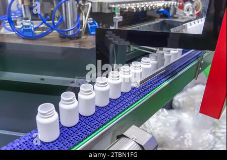Moving polypropylene white bottles on conveyor belt of automatic liquid filling machine Stock Photo