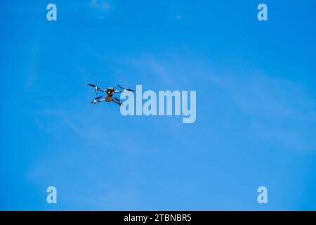 drone flying against a clear blue sky, symbolizing modern technology and surveillance. Stock Photo