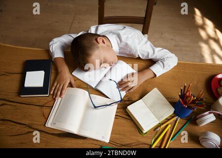 Overhead view on exhausted little schoolboy sleeping on desk table Stock Photo
