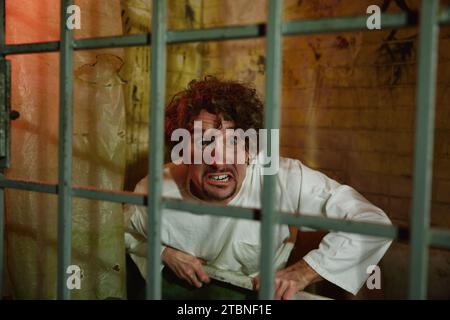 Crazy forsaken man sitting in bathroom behind cage gate Stock Photo