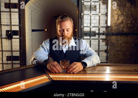 Portrait of thoughtful elegant man looking at glass of whiskey Stock Photo