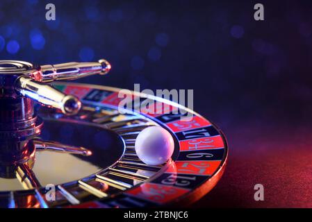 Detail of ball fixed on the black six of a casino roulette wheel on table and dark isolated background with soft red and blue lighting in the dark. Stock Photo