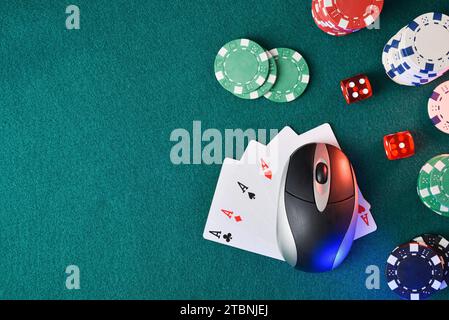 Online casino gaming concept with computer mouse over playing cards and dice and betting chips around on green mat. Top view. Stock Photo