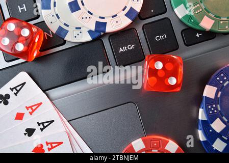 Concept of playing online casino games with detail of betting chips, poker cards and dice on gray laptop keyboard. Top view. Stock Photo