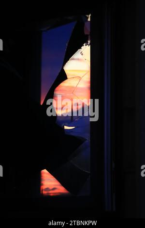 Beautiful sunset sky reflected in glass shards of a broken window. Stock Photo