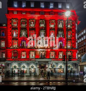 A tourist shelters under an umbrella, as they admire the advent calendar facade of the famous landmark of Fortnum & Mason. Stock Photo