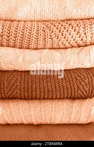Stack of warm cozy knitted women's sweaters. Cozy autumn or winter clothes. Image toned in trendy color of year 2024 Peach Fuzz. Closeup. Stock Photo