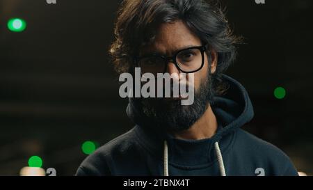 Male portrait serious confident bearded Indian 30s millennial business man in eyeglasses looking to side turn head at camera at dark parking lot Stock Photo