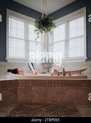 Woman relaxing in a bubble bath in deep tub with a book. Stock Photo