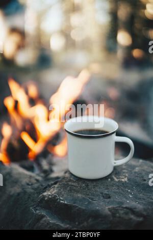 White Coffee Cup Next to a Camp Fire Stock Photo