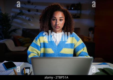 Portrait serious young afro woman looking concentrated at camera sitting in front laptop at home.  Stock Photo